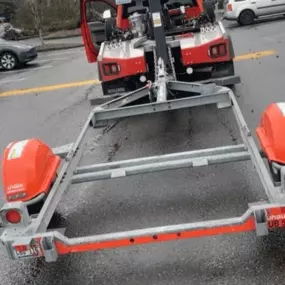 A red tow truck is parked on a wet street with a U-Haul car trailer attached, surrounded by vehicles and buildings.