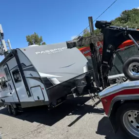 A red tow truck is towing a gray Passport SL Series travel trailer in a parking lot under a clear blue sky.
