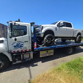 A Choice Towing flatbed truck is transporting a white pickup truck on a sunny day. The tow truck's logo and phone number are visible.