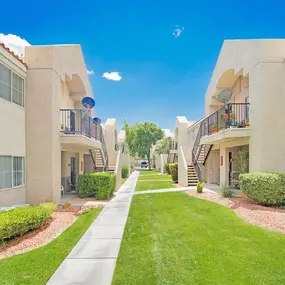 Lush walkway between apartment buildings with balconies and green grass