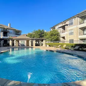Resort-style swimming pool surrounded by green bushes and lounge chairs in the shade
