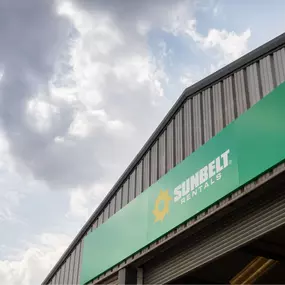 Exterior view of a Sunbelt Rentals depot showing the green signage with the yellow sunburst logo and white company name.