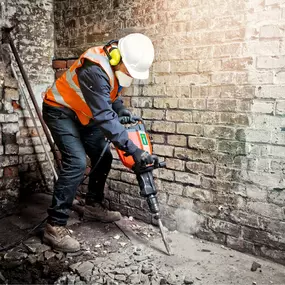 Construction worker using a heavy-duty breaker tool while wearing PPE and high-visibility clothing.