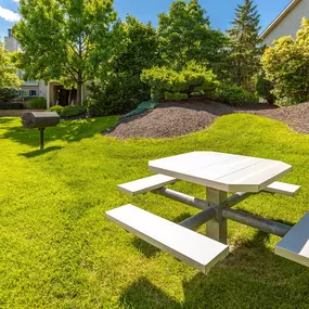A picnic table sits in a grassy area with trees and a building in the background.