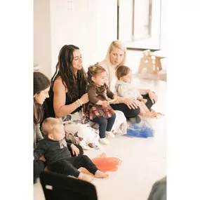 New moms sit on the floor with their infants learning from the class instructor