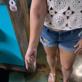 A woman shows off a fresh forearm tattoo of a hand making the 