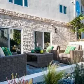 A cozy outdoor seating area features dark wicker furniture with plush cushions. The patio is set against a textured brick wall with sliding glass doors, creating a perfect spot for relaxation and entertaining.