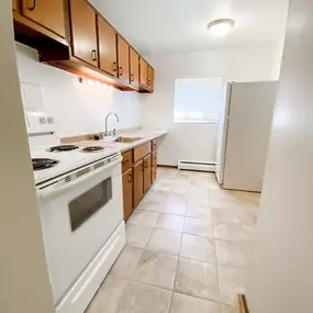 An empty kitchen with white appliances and wooden cabinets