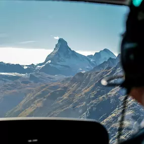 This photo captures a unique moment from one of our FunFlights helicopter tours to the iconic Matterhorn. Taken from the back seat, the image shows part of the cockpit and our pilot in action, with the world-famous peak in the distance. Starting from the