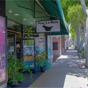 Pour Le Bain boutique in Uptown Whittier, featuring its signature green canopy, classic bathtub logo, and an inviting display of lush plants along the sidewalk. A charming destination for skincare, gifts, and botanical treasures.