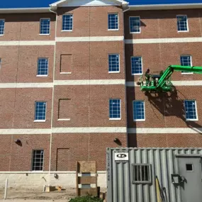 Sandblasting and painting crew on boom lift working on exterior of a multi-story brick building.