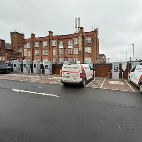 A wide-angle view showing the full row of InstaVolt ultra-rapid chargers in use, with branded InstaVolt vans parked in the charging bays at the Apex Retail Park site in Birmingham.