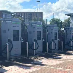 This side-angle photo captures multiple InstaVolt chargers in a row, with clear EV-only markings and brick paving, set against a bright blue sky at the Dunelm site in Birmingham.