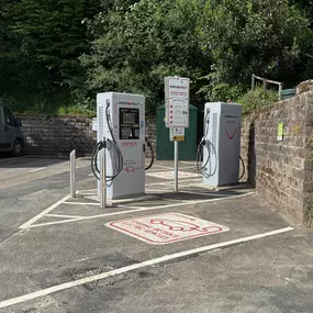 Close-up of InstaVolt’s electric vehicle chargers in Glen Lyn Car Park, nestled against a stone wall and lush greenery. Painted bays and a clear instruction sign for EV charging.