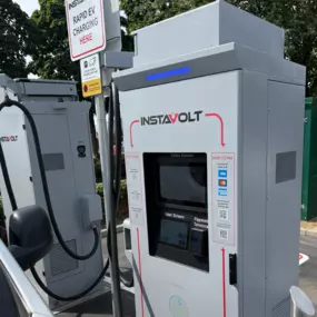 Close-up of an InstaVolt ultra-rapid EV charger in a tree-lined area, featuring contactless payment options and clear user instructions.