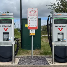 Straight-on view of two InstaVolt EV chargers with instructional signage in the centre, surrounded by greenery and open space.