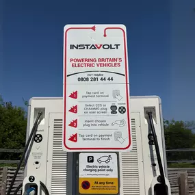 A clear view of the user instructions on an InstaVolt EV charging unit located at McDonald’s Bridgwater Business Park. The signage explains how to use the contactless payment system and select either CCS or CHAdeMO connectors, with a backdrop of blue sky and greenery, enhancing visibility and simplicity for EV drivers.
