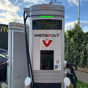 A front-facing view of an InstaVolt charger in use, showing ChargePoint branding and contactless payment instructions, with the McDonald’s logo visible in the background.