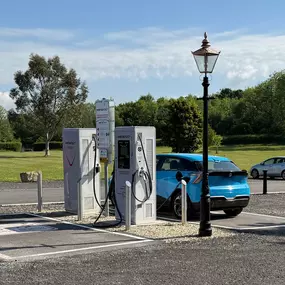 A wide-angle shot showing an electric vehicle charging at one of the InstaVolt units, set against an open green space with rural surroundings and clear weather.