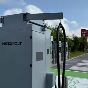 A detailed close-up of an InstaVolt ultra rapid charger shows cable management and connector ports, set against the backdrop of the charging bay layout. The nearby KFC signage highlights a convenient food option for EV drivers while charging at the Wincanton A303 location.