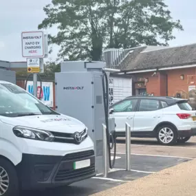 The image shows InstaVolt ultra-rapid chargers in operation outside the Co-op store on Bedford Road, Barton-le-Clay. Multiple vehicles, including an InstaVolt van, are parked and charging.