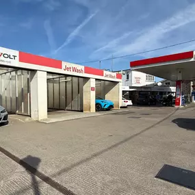This image shows the forecourt of Braunton Service Station on the A361, featuring InstaVolt rapid EV chargers housed in dedicated charging bays next to Jet Wash units. An Esso fuel station canopy is visible to the right, with several parked cars.