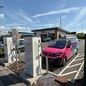 This wide-angle photo displays the full InstaVolt charging setup outside Costa Coffee in Bristol. A branded Octopus Energy van is charging, and Greggs is visible in the distance. The image captures the convenient co-location of EV charging, food, and drink amenities for EV drivers.
