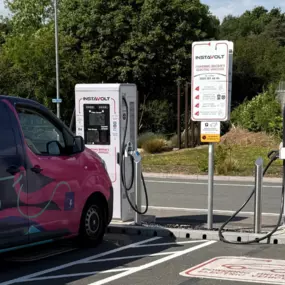 A pair of InstaVolt ultra rapid chargers are seen in active use with a brightly branded Octopus Energy van parked in one bay. The area is neatly marked with EV charging signage and surrounded by greenery under a blue sky, representing a well-maintained charging facility.