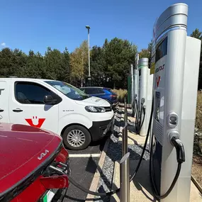 A dedicated InstaVolt van is seen charging at a rapid charger bay in a clean, open location. The site is surrounded by trees and offers easy-to-spot, clearly signed charging units.