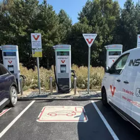 A clear view of InstaVolt’s rapid and ultra-rapid chargers in use, located at a tree-lined charging site. The charging bays are clearly marked and show both cars and a branded InstaVolt van plugged in.