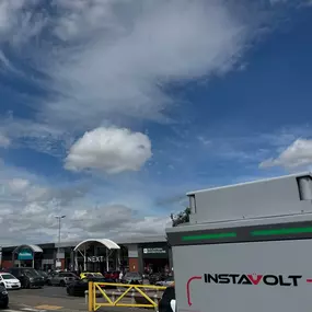 An InstaVolt charger is seen in the foreground, with a wide view of Gallagher Retail Park’s retail offering including Next, Mountain Warehouse, and Poundland.