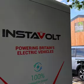 Detailed view of an InstaVolt charger displaying the ‘100% renewable power’ label, with Three Trees Farm Shop’s logo visible on the building behind.