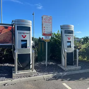 Twin InstaVolt chargers in a well-marked bay with clear signage and nearby vegetation.