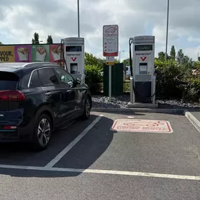 Kia EV charging at InstaVolt units near a McDonald’s drive-thru, surrounded by bushes and clear bay markings.
