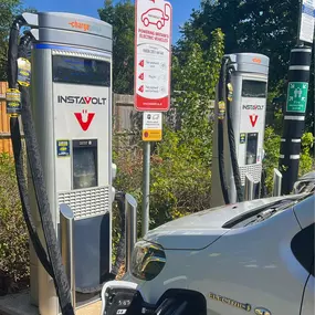 Two InstaVolt EV chargers with clear signage and a white electric car charging on site. The area is marked with safety notices, set against a backdrop of trees and fencing in Shirley.