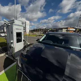 A black EV is connected to an InstaVolt charger at McDonald’s Fairhill, Bedford. The McDonald’s restaurant is clearly visible behind the charging area.