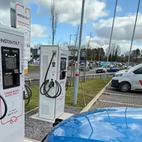A blue electric vehicle charges at InstaVolt’s Rugeley location, with Aldi signage in the background and an InstaVolt service van parked nearby.