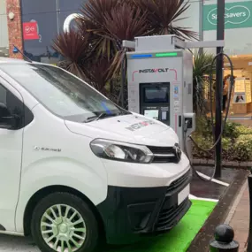 An InstaVolt charger is in use outside Holland & Barrett and Specsavers, with an electric van charging in a marked EV bay.