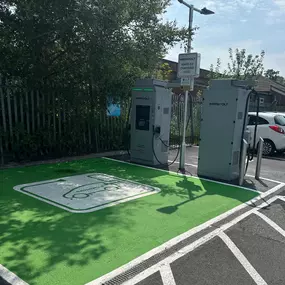 This image shows InstaVolt ultra rapid electric vehicle chargers at Spendmore Lane in Coppull. The charging bays are clearly marked with EV graphics, supported by visible InstaVolt branding and a “Rapid EV Charging Here” sign.