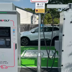A pair of InstaVolt ultra rapid EV chargers at a Coppull site, located beside a wooden fence and trees. The green-painted accessible bay with a large EV symbol with InstaVolt signage and branding.