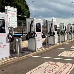 A clean and modern InstaVolt charging site featuring multiple ultra-rapid chargers and EV-dedicated parking bays, set against a tree-lined background.