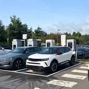 EVs charging at InstaVolt ultra-rapid chargers in a well-marked car park with a tree-lined background and clear weather.
