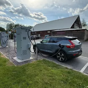 An electric Volvo is shown plugged into one of InstaVolt’s ultra rapid chargers at Cobbs Farm Shop. The farm shop building can be seen in the background, confirming the convenient access to local food and shopping during a charge.