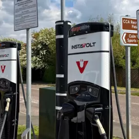 A close-up view of two InstaVolt rapid EV chargers at Culm Valley Sports Centre, clearly signposted for electric vehicle use only. Surrounding signs include usage instructions and a pointer to the nearby recreational fields.