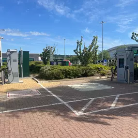 Two InstaVolt chargers are located in a clean retail park environment, with trees and a visible Asda store in the background.