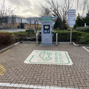 A single InstaVolt rapid charger is installed in a dedicated EV bay surrounded by bare trees and retail buildings in the background.