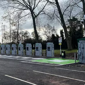 Wide-angle view of multiple InstaVolt EV chargers positioned near trees with dedicated green and white EV parking spaces.