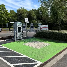 A single InstaVolt charger in the foreground sits in a green-marked charging bay, with several more chargers and two InstaVolt-branded vans visible across the car park.