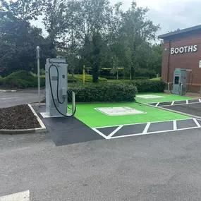A pair of InstaVolt chargers with vibrant green EV-only bays located outside a Booths store. Surrounded by trees and hedges, offering a convenient stop for shoppers needing a charge.