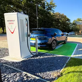 Close-up of an EV charging cable connected to a BMW electric vehicle with a Fitness First gym visible in the background.